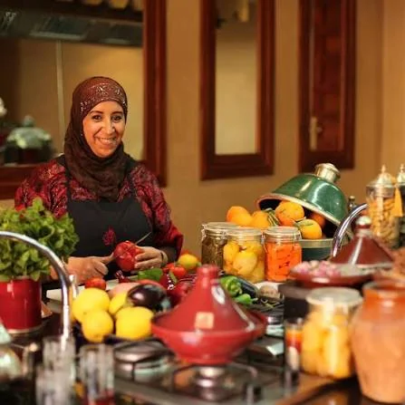 A Dada preparing a Moroccan meal surrounded by tajines and fresh produce