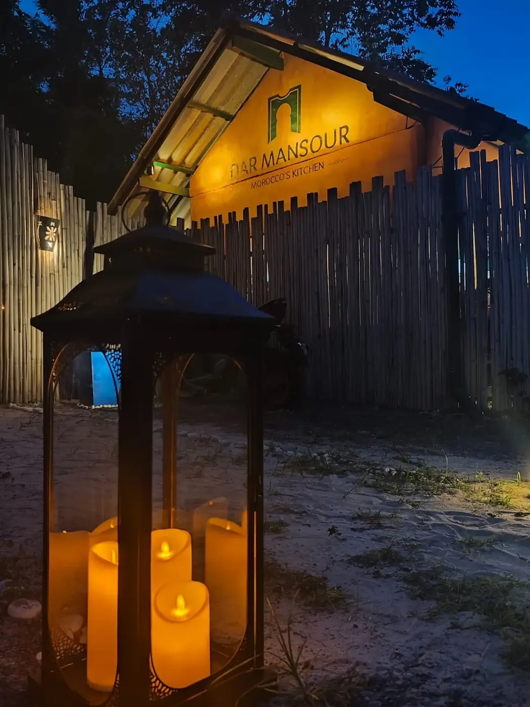 The illuminated Dar Mansour entrance sign with a Moroccan candle lantern at dusk in Koh Phangan