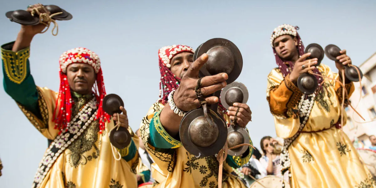 Gnaoua musicians in traditional costume and cowrie-shell caps playing krakebs (iron castanets) at a festival in Morocco