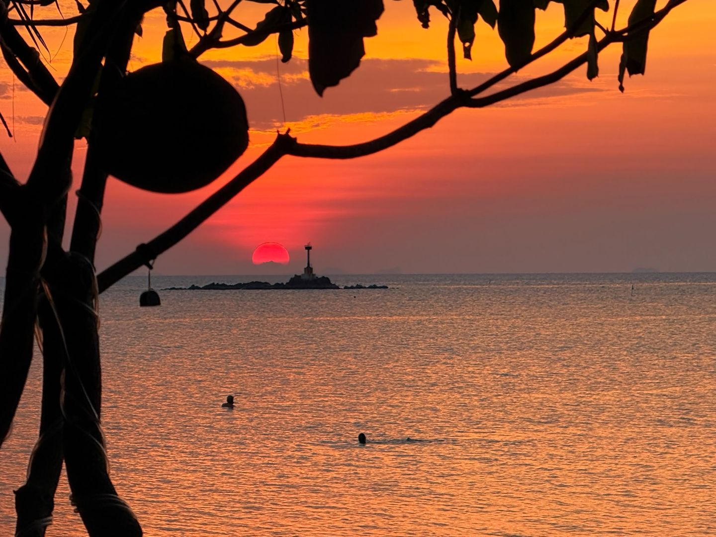 Red sun setting over Zen Beach, Koh Phangan The sun setting as a deep red disc behind the offshore beacon, framed by trees at Zen Beach, Koh Phangan